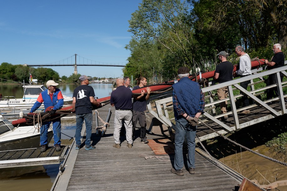 Le mât, long de 6,30 mètres et d’un diamètre de 20 centimètres à la base, pèse son poids : dans les 140 kilos ! Le transporter sur le ponton puis dans la barque sans emmêler le gréement n'a pas été simple. Mais ce n'était que le début ! © www.tessier.photos